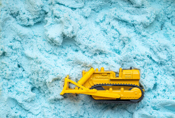 Toy yellow, cargo bulldozer on a blue background made of magnetic sand. Toy and industry.