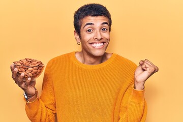 Young african amercian man holding bowl with almonds screaming proud, celebrating victory and success very excited with raised arm