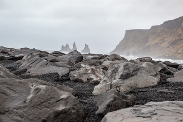 Obraz premium Black stones with large rock formations in the background in Iceland.Reynisfjara black sand beach in Iceland at winter. Famous Reynisdrangar rock formations at black Reynisfjara Beach.