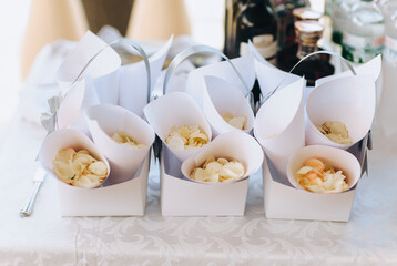 Fototapeta na wymiar Rolled paper cone packages with white rose petals on the table close-up. Wedding ceremony. Photography, concept.