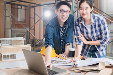 consulting meeting of two smart male female asian interior designer or achitect with blueprint home mockup and material sample with happy at house renovate improvement site construction background