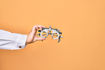 Hand of caucasian young woman holding optometry glasses over isolated yellow background