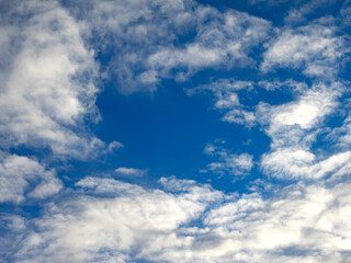 Light puffy cotton wool like cumulus clouds framing a central blue sky area