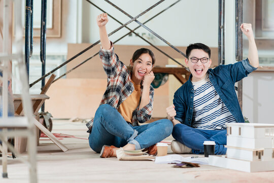 Cheerful asian couple hand rise up with successful and happiness renovating the house site construction background