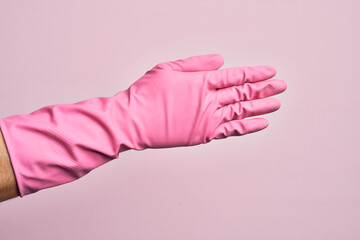 Hand of caucasian young man with cleaning glove over isolated pink background stretching and reaching with open hand for handshake, showing back of the hand