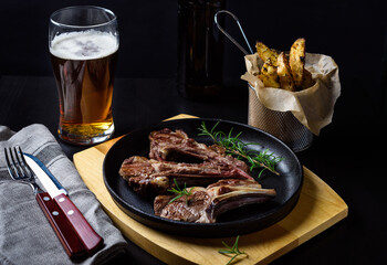 Grilled lamb chops in a cast-iron frying pan with fried potatoes and glass of beer on dark background © Ekaterina Belova
