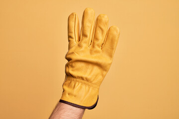 Hand of caucasian young man with gardener glove over isolated yellow background counting number 4 showing four fingers