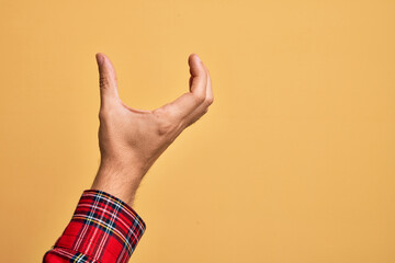 Hand of caucasian young man showing fingers over isolated yellow background picking and taking invisible thing, holding object with fingers showing space