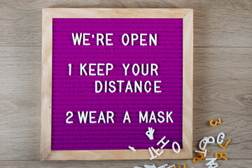 Obraz premium We're open, keep your distance, wear a mask text on purple letter board near the notebook. Business concept. Service, restaurant, shop and cafe. Reopening of the place after the quarantine covid-19.