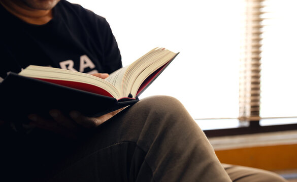 young man is sitting reading in the window in the room with soft-focus and over light in the background
