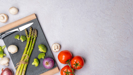 Group of organic fresh vegetables - green asparagus, broccoli, mushrooms on grey background, flat lay. Concept of  healthy vegetarian food, diet and home cooking. Top view, copy space.