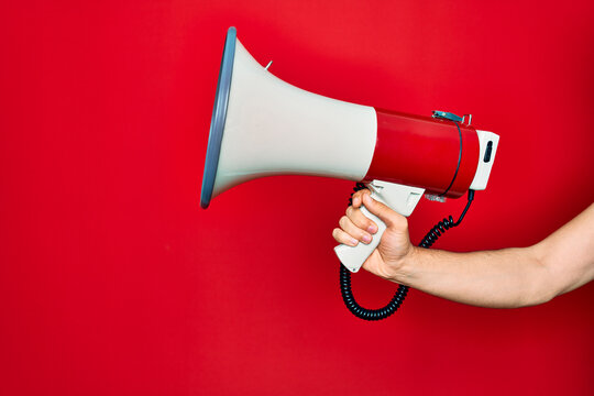 Beautiful hand of man holding megaphone over isolated red background