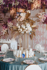 Banquet table with blue velvet tablecloth, candles, Alexa Dining Chair. High stand with a composition of rose flowers, hydrangeas, golden leaves. Against the background of golden racks with flowers, s