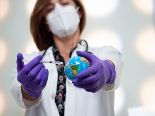 Doctor wearing a medical mask and medical gloves injecting a vaccine into a world globe