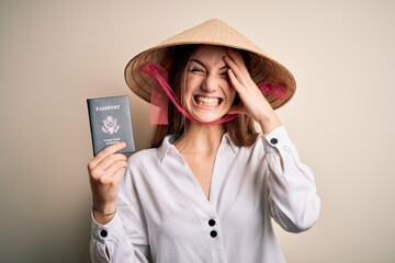 Young beautiful redhead tourist woman wearing asian traditional hat holding usa passport stressed with hand on head, shocked with shame and surprise face, angry and frustrated. Fear and upset