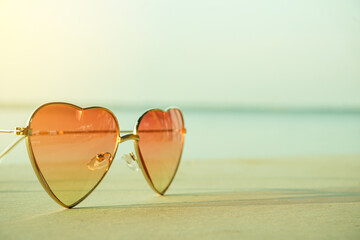 Fototapeta na wymiar Beautiful heart shaped fashion glasses placed on the beach floor and background sea blur