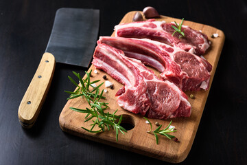 Raw lamb chops on a wooden cutting board with spices on a dark wooden background