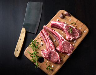 Raw lamb chops on a wooden cutting board with spices on a dark wooden background