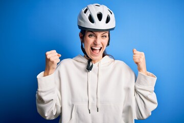 Young beautiful redhead cyclist woman wearing bike helmet over isolated blue background celebrating surprised and amazed for success with arms raised and open eyes. Winner concept.