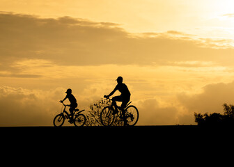 silhouette elder and brother riding bicycle in evening