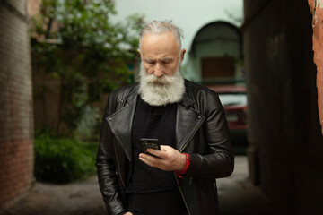 Bearded senior man texting on phone. Casual urban professional entrepreneur using smartphone outside.