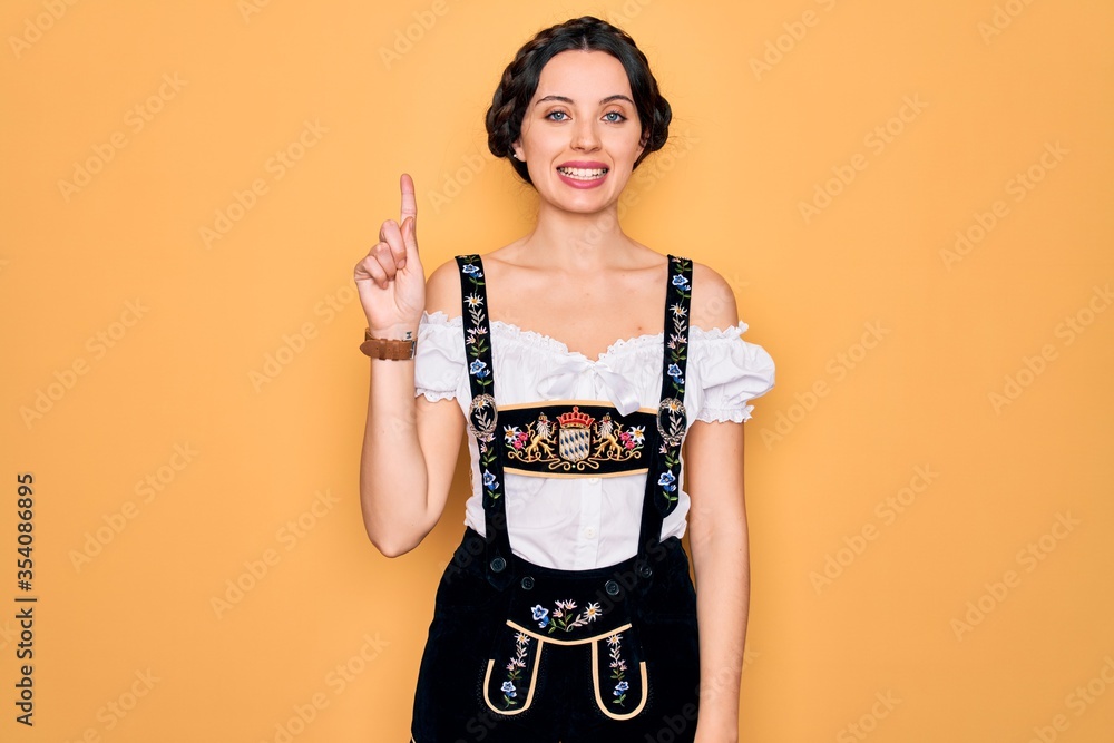 Wall mural Young beautiful german woman with blue eyes wearing traditional octoberfest dress showing and pointing up with finger number one while smiling confident and happy.