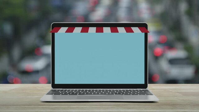 Modern laptop computer with online shopping store graphic and open sign on wooden table over blur of rush hour with cars and road in city, Business internet shop online concept