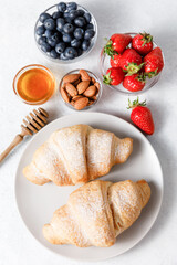 Delicious breakfast with fresh croissants, honey, berries on white table background.