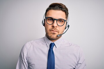 Young call center operator business man with blue eyes wearing glasses and headset with serious expression on face. Simple and natural looking at the camera.