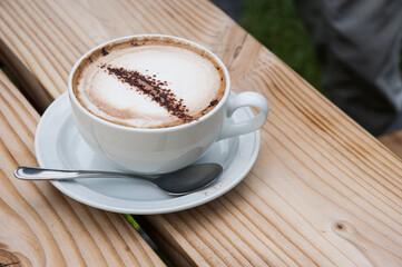 A cup of Cappuccino on top of a wooden bench table