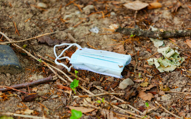 Obraz premium Facial surgical mask used and thrown away on the ground in the park. True and authentic image of a dirty mask.
