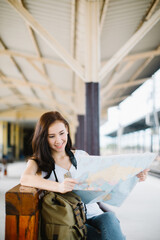 Beautiful woman traveler holding location map in hands and sitting at train station