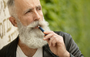 Electronic Cigarette Technology. Tobacco IQOS system. Close-up of a bearded senior man smoking an electric hybrid cigarette with a heating pad.