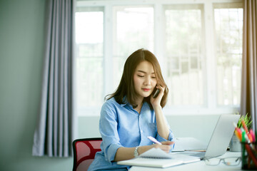 Obraz premium Beautiful young Asia woman working with laptop and smart phone in living room