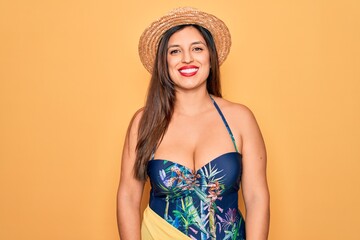 Young hispanic woman wearing summer hat and swimsuit over yellow background with a happy and cool smile on face. Lucky person.