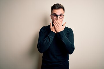 Young handsome caucasian man wearing glasses and casual sweater over isolated background shocked covering mouth with hands for mistake. Secret concept.