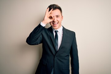 Young handsome business man wearing elegant suit and tie over isolated background doing ok gesture with hand smiling, eye looking through fingers with happy face.