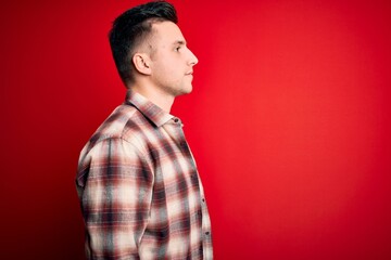 Young handsome caucasian man wearing casual modern shirt over red isolated background looking to side, relax profile pose with natural face and confident smile.