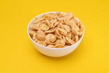 White plate with cornflakes for a delicious breakfast on a yellow background.