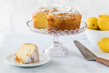 A lemon curd bundt cake on a cake stand with a slice of cake on a plate ready for eating.