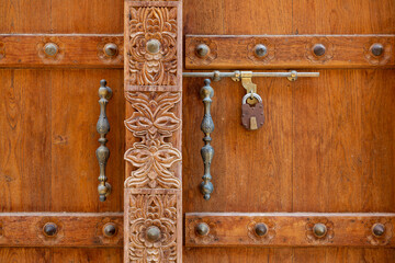 Detail of brown wooden door with carvings and metal handles in old town of Al Mudairib, Oman