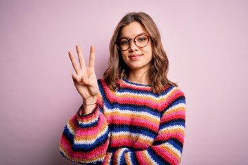 Young beautiful blonde girl wearing glasses and casual sweater over pink isolated background showing and pointing up with fingers number three while smiling confident and happy.