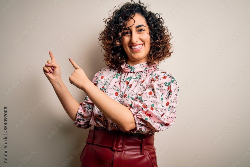 Wall mural young beautiful curly arab woman wearing floral t-shirt standing over isolated white background smil