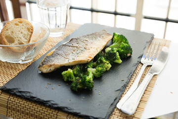 fried fillet of sea bass with garnish of broccoli on black warm stone plate