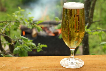 glass glass with cold beer on a warm evening in nature. beer on the background of a burning fire in the grill