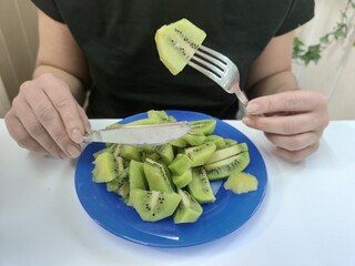 girl eating a fork of kiwi from a blue plate