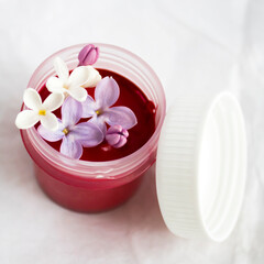 White and violet lilac flowers in a jar of ruby red gouache or acrylic paint on white paper backdrop. Still life photo. Artist's life style. For art blogger and influencer. Beautiful spring picture