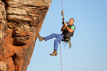 Photographer and rock climber Norbert Frank taking pictures in while hanging in front of a rock