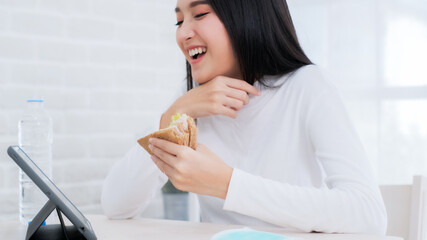 Woman Using Digital Tablet At Home.Young Asian woman working with tablet at home and eating sandwich salad fruits at home