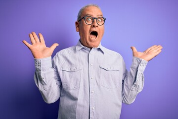 Middle age handsome hoary man wearing striped shirt and glasses over purple background celebrating...